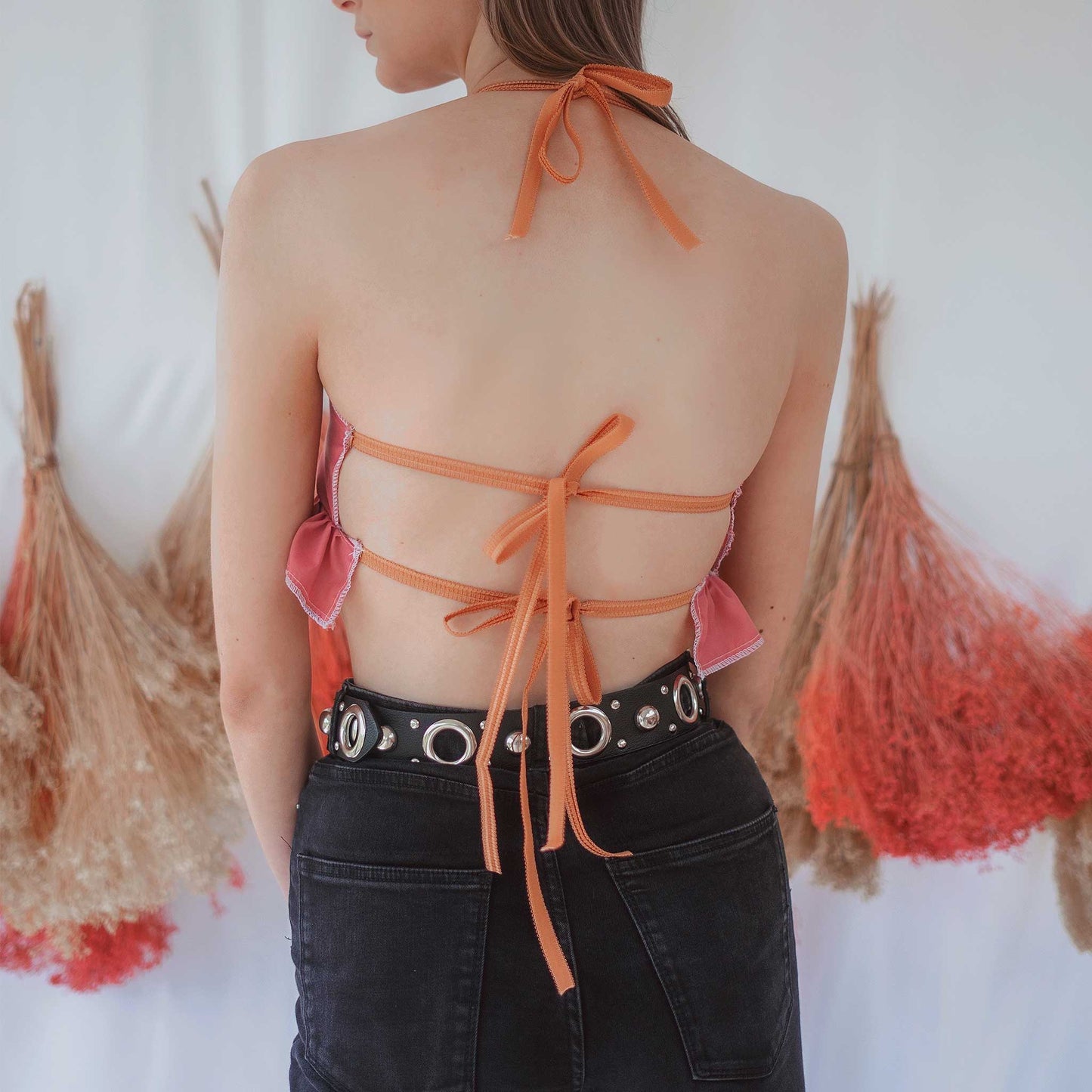 Fashion model wearing dusky pink coloured backless bralette with gathered frill under bust, and orange elasticated straps at neck and back.