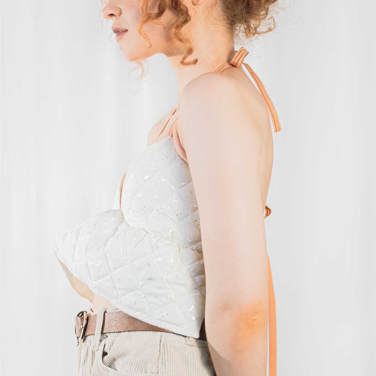 Fashion model wearing cream quilted backless bralette with orange elasticated straps at neck and back.