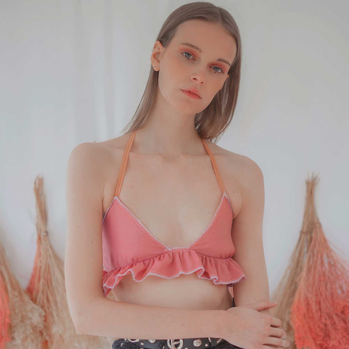 Fashion model wearing dusky pink coloured backless bralette with gathered frill under bust, and orange elasticated straps at neck and back. 