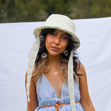 Load image into Gallery viewer, Fashion model wearing cream quilted bucket hat with fabric straps to tie around the neck.
