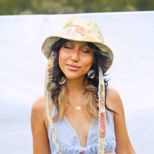 Load image into Gallery viewer, Fashion model wearing beige floral bucket hat with fabric straps to tie around the neck.
