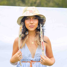 Load image into Gallery viewer, Fashion model wearing beige floral bucket hat with fabric straps to tie around the neck.
